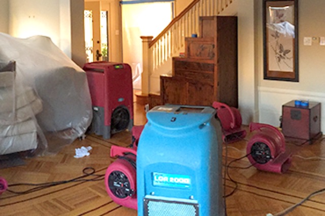 Air movers and a dehumidifier drying a water-damaged living room